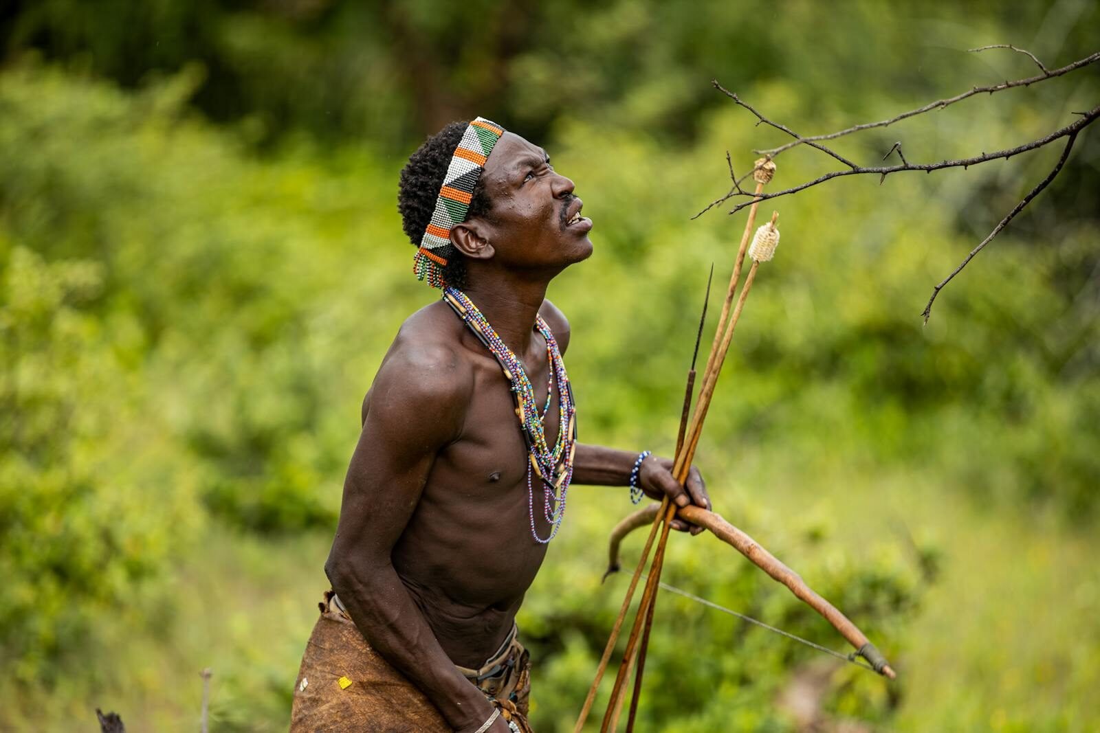 Portrait of a traditional hunter with a bow, set in lush greenery, capturing cultural heritage.